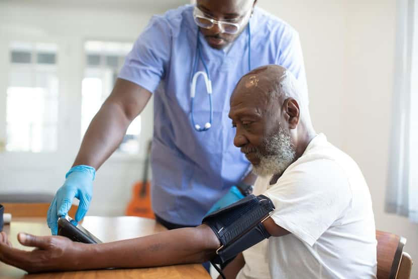A nurse checking an older man's blood pressure at his dining table