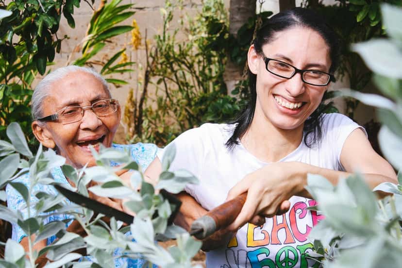 A woman and an older woman laughing together while gardening outdoors